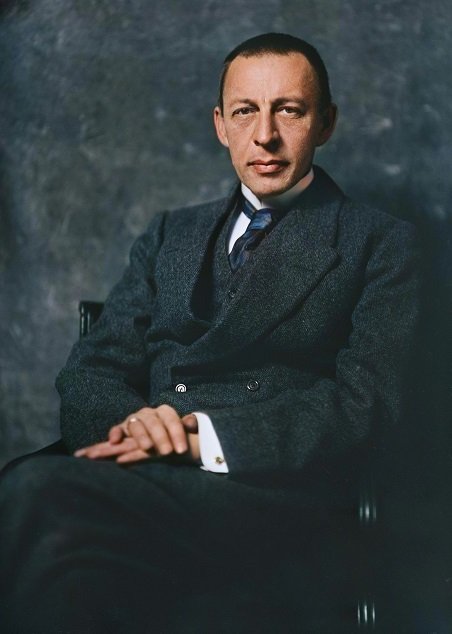 licensed-image Portrait of a man in a dark suit seated in a studio chair, hands folded on his lap and looking at the camera.