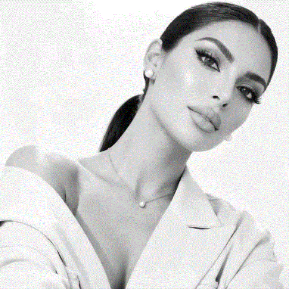 Black-and-white portrait of a woman with slicked-back hair, bold makeup, wearing a blazer and pearl necklace.