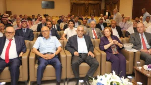 0c08cfb0-a830-4fb2-a47f-5eeb7c62f60c - عروبة الاخباري | Oroba News Large indoor conference with a diverse audience seated in rows; front row shows men in suits and a woman in purple, attentive to the event.