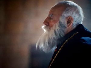 3-2-300x225 - عروبة الاخباري | Oroba News Profile view of an elderly man with a long white beard wearing a dark robe and a gold chain, looking to the right.