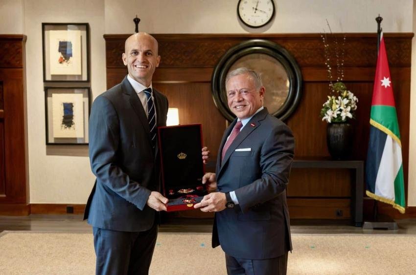 Two suited men in a formal office pose as one presents an open red box with medals to the other, Jordan flag in the background.
