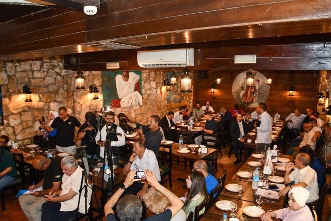 333000000099990 - عروبة الاخباري | Oroba News Crowded rustic restaurant with many diners, a camera on a tripod, and guests taking photos at a social event.