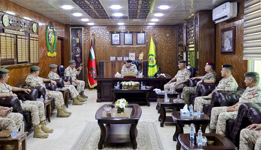 639214429539032402 Group of military officers in camouflage uniforms seated along both sides of a wood-paneled conference room.