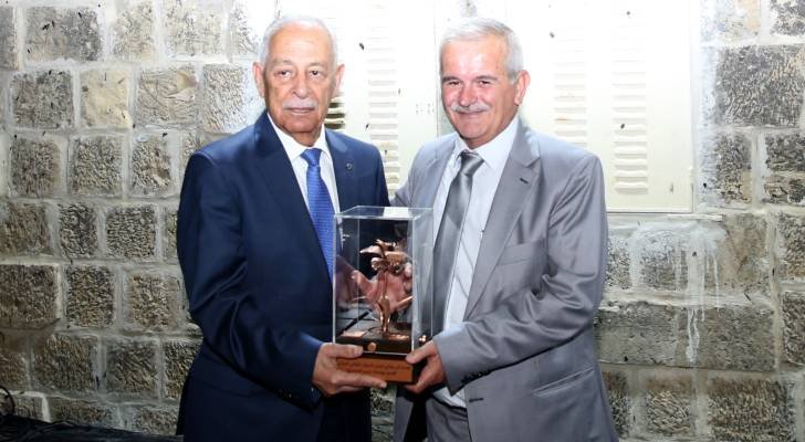 6a6ce677409701785521783 Two men in suits pose with a glass award trophy in front of a stone wall.