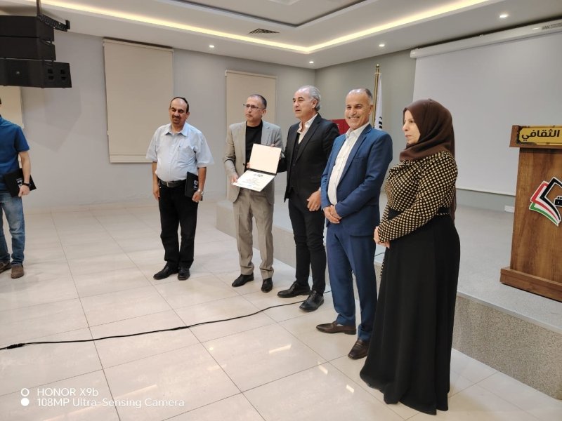 6a73a844bff4b - عروبة الاخباري | Oroba News Group of six people on a stage during an award ceremony; one man holds an open certificate folder while others pose nearby, a podium with a logo to the right.