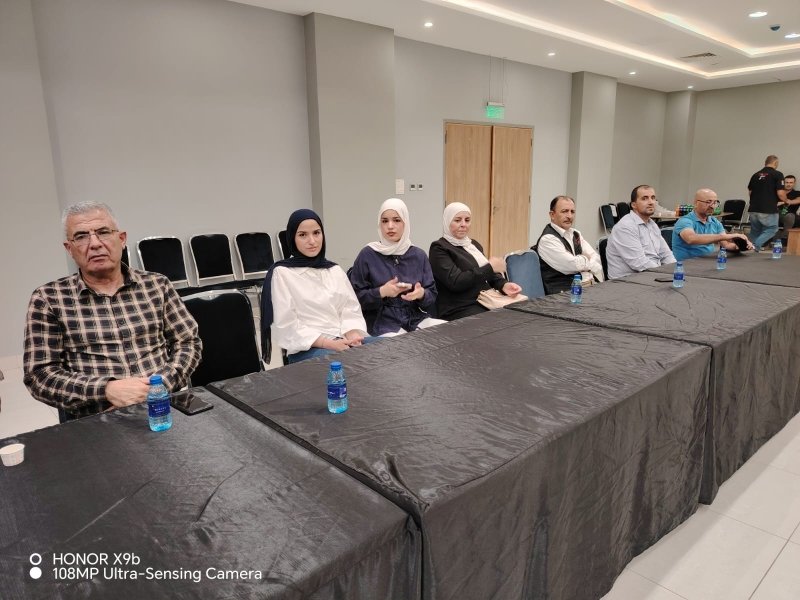 6a73a844db8dc - عروبة الاخباري | Oroba News Eight people sit along a long conference table covered with a black tablecloth in a neutral meeting room; water bottles are on the table.