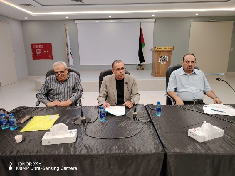 6a73a84512688 - عروبة الاخباري | Oroba News Panel of three men seated at a long black table in a conference room, microphones and papers in front of them, Jordan flag in the background.