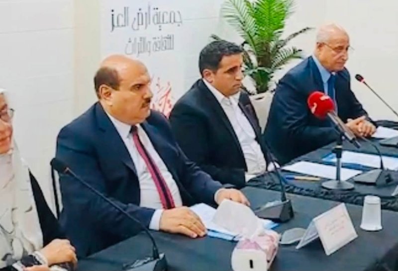 6a74778bd9b27 - عروبة الاخباري | Oroba News Panel of men in suits seated at a conference table with microphones, papers, and name cards, speaking into mics as an audience watches; Arabic banner in the background.