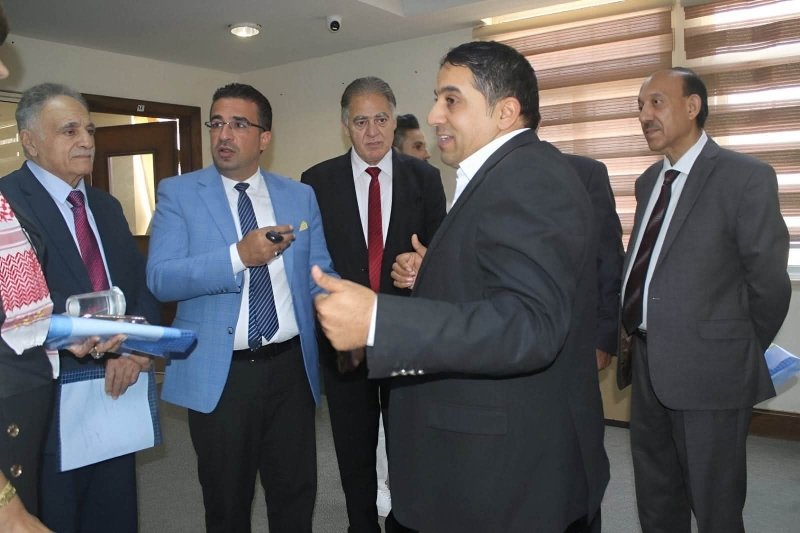6a74778c1a219 - عروبة الاخباري | Oroba News Group of five men in business suits standing in a hallway, one man speaking and gesturing as others listen.