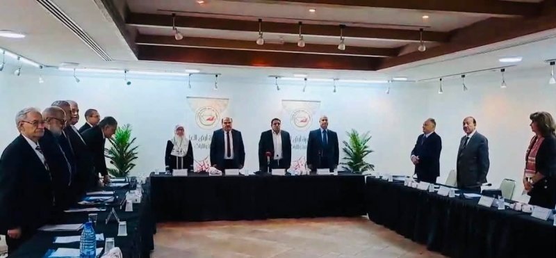 6a74778c26628 - عروبة الاخباري | Oroba News Group of officials standing around a U-shaped conference table in a bright meeting room, with a central speaker addressing the others and banners in the background.