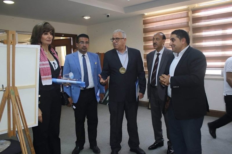 6a74778c5a87b - عروبة الاخباري | Oroba News Five professionals stand in a room with display boards; a woman on the left holds a rolled certificate while a man with a gold medallion speaks to the group.