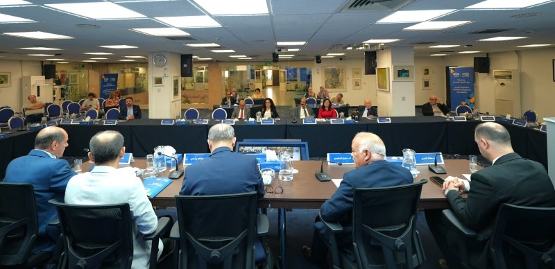 6a772a3506c18 - عروبة الاخباري | Oroba News Formal boardroom meeting with professionals seated around a long U-shaped table; water bottles and name placards visible.