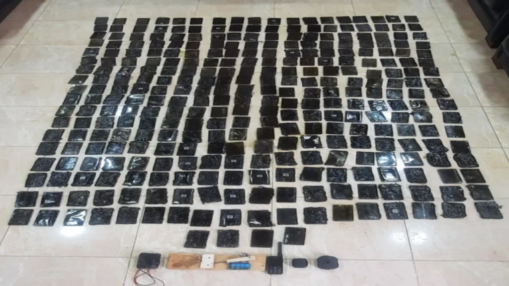 Dozens of small black rectangular packets arranged in a grid on a tiled floor, with a radio and other devices at the front.