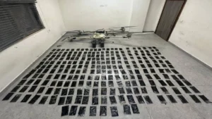 Indoor room with a large drone placed near the back wall and dozens of black rectangular cards arranged in neat rows across the tiled floor, like a grid.