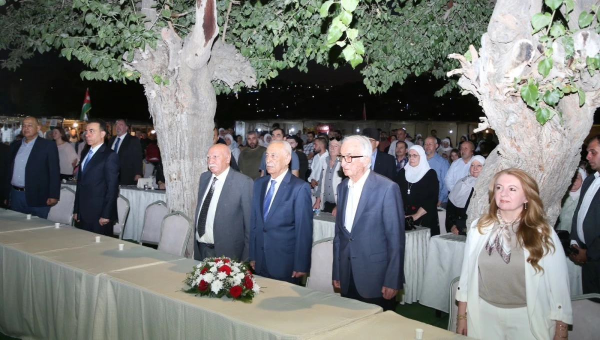 759331 Group of formally dressed people standing behind a long table with a floral centerpiece at an outdoor ceremony under trees at nightfall.