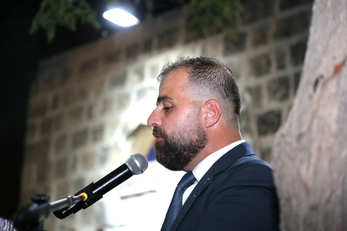 759334 Bearded man in a navy suit speaks into a microphone outdoors at night.