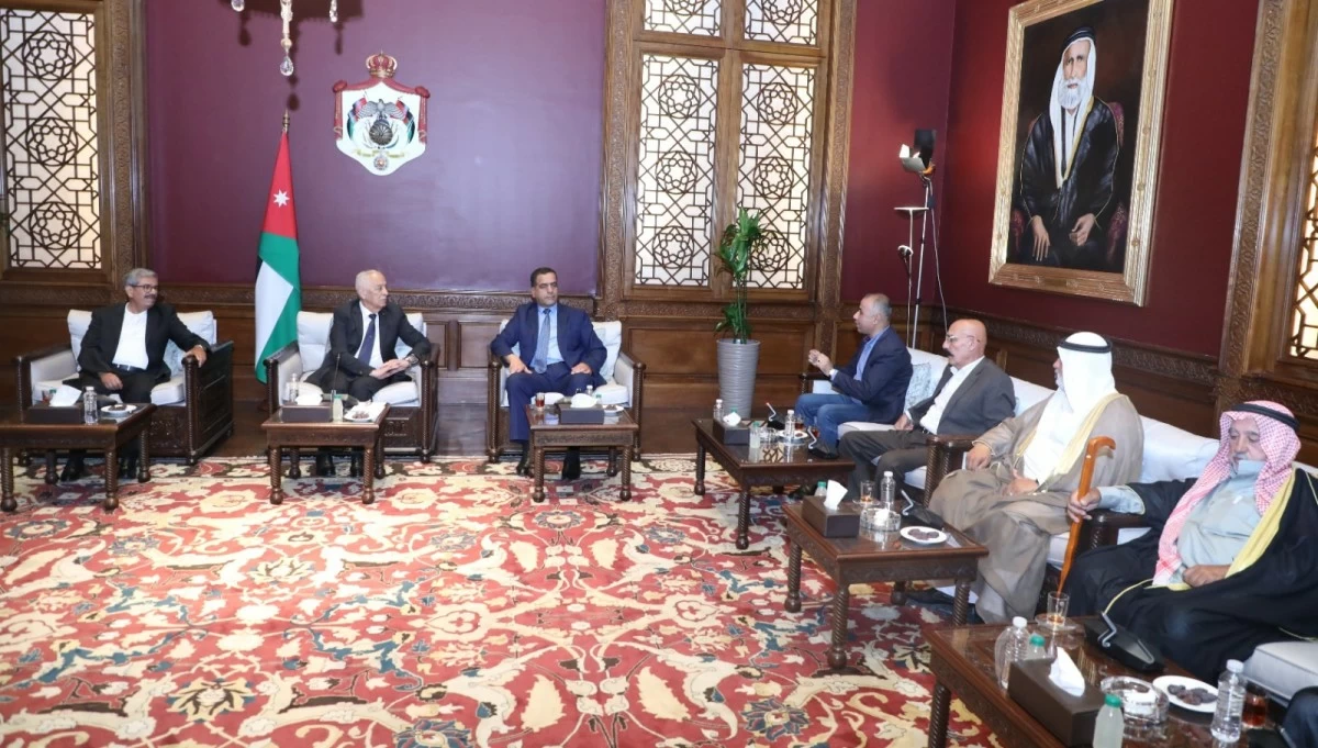 760735 - عروبة الاخباري | Oroba News Formal meeting in a richly decorated room: seven men seated in armchairs around small tables, a Jordanian flag visible in the background, and a large portrait on the wall.