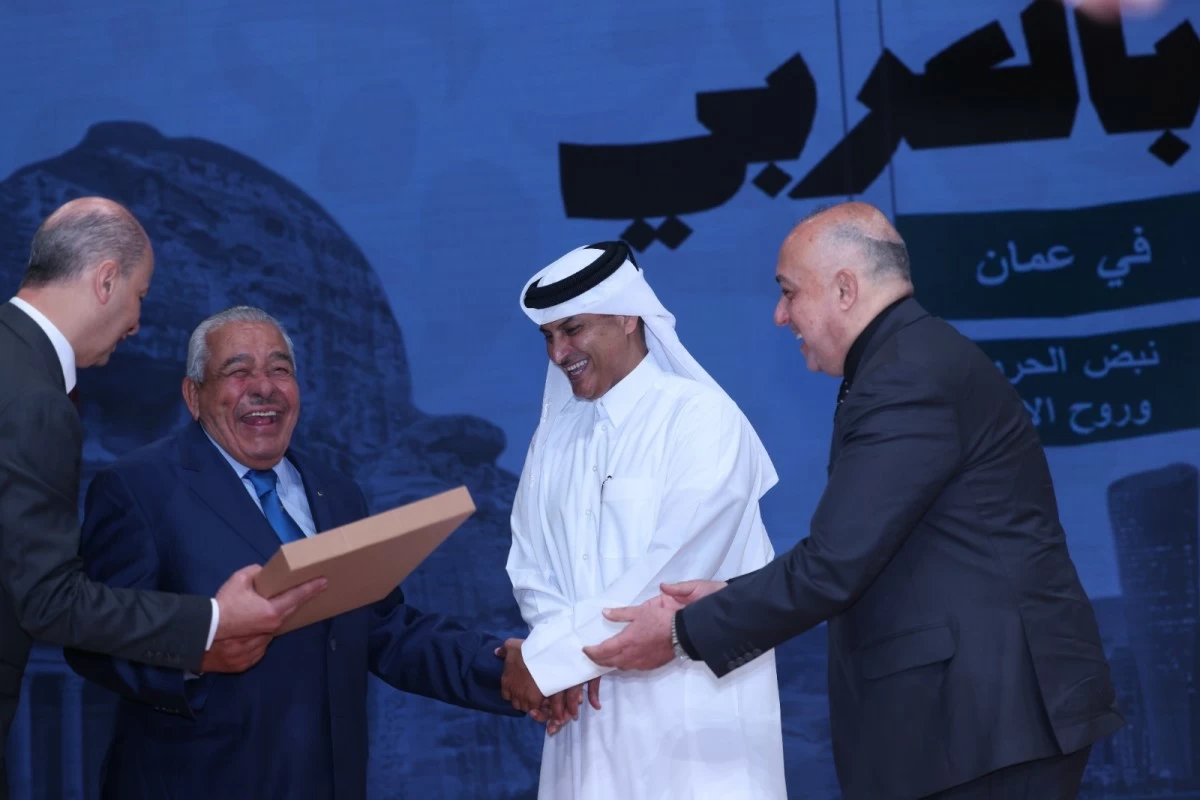 760755 - عروبة الاخباري | Oroba News Four men in suits on a stage shake hands; one is handed a rectangular award box by another.