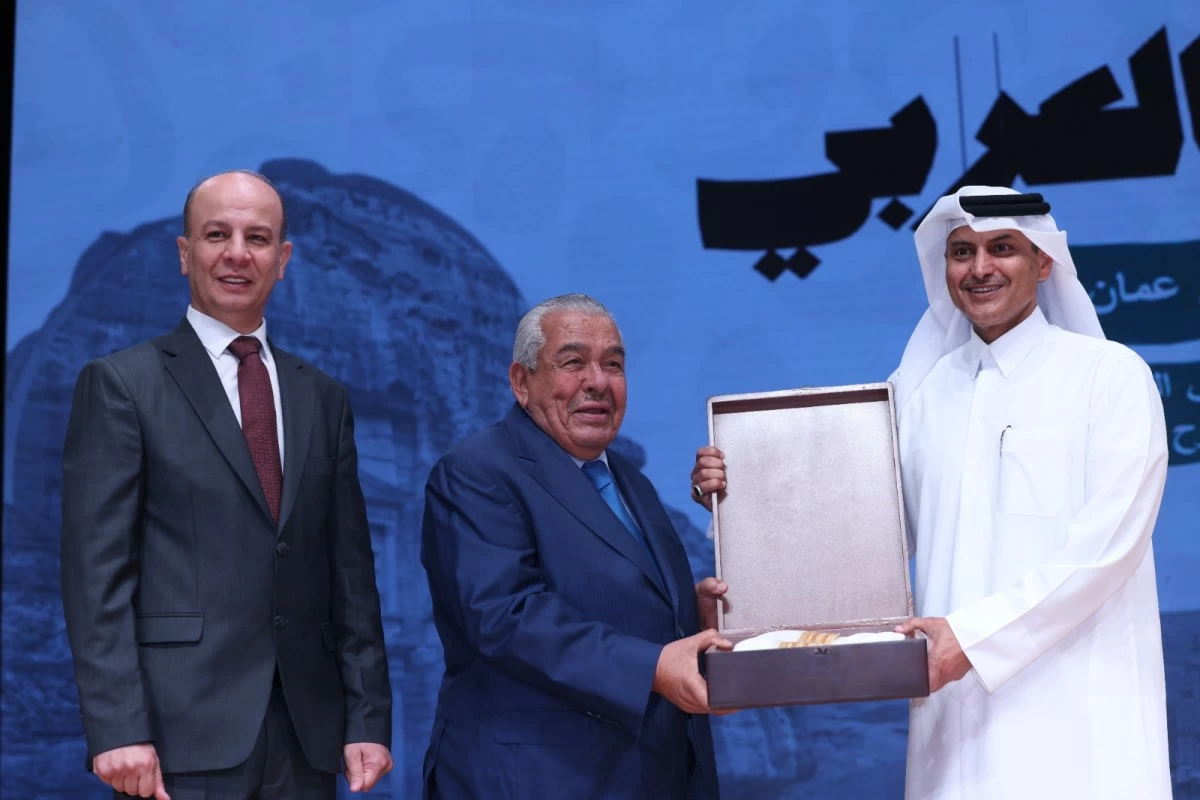760757 - عروبة الاخباري | Oroba News Three men on a stage as one in a dark suit presents a boxed award to a man in a white thobe, another man watches.