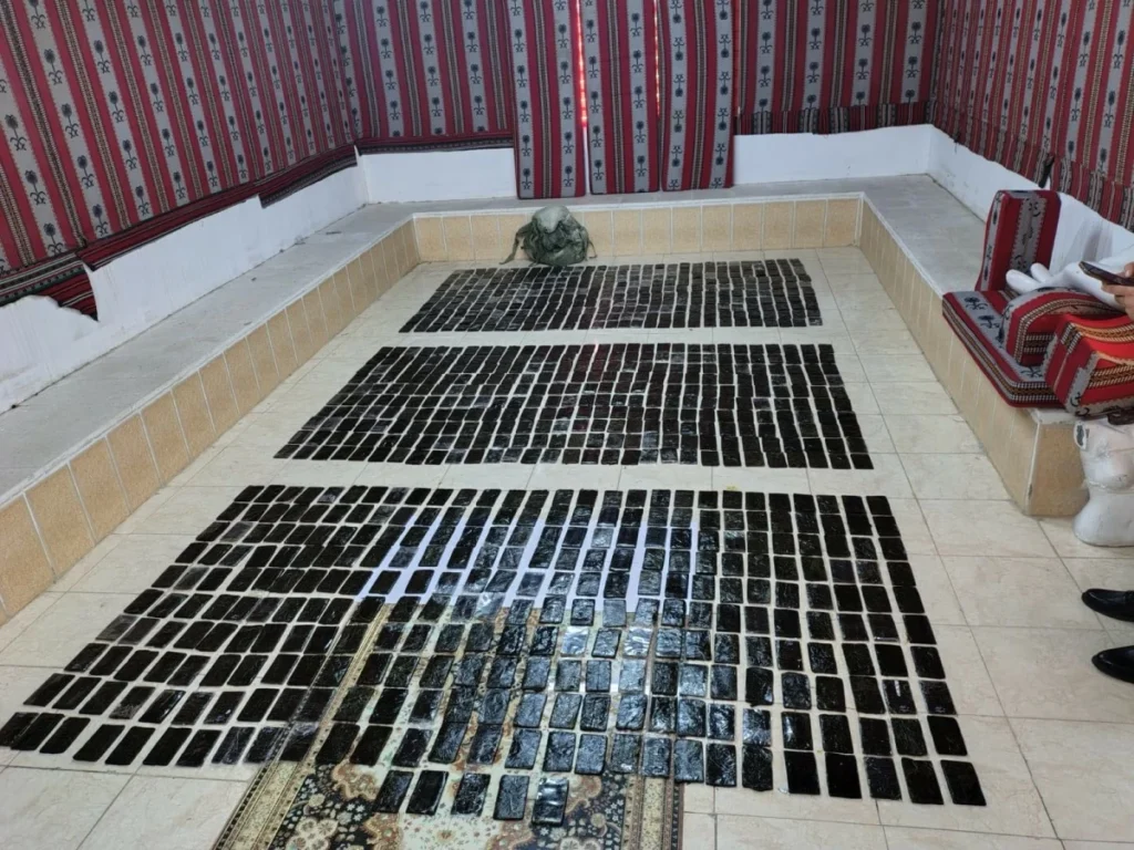 760779 - عروبة الاخباري | Oroba News Room with hundreds of black rectangular tiles arranged in neat rows on a tiled floor; patterned red textiles cover the walls and a person sits on the right using a phone.