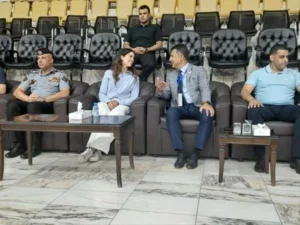 761080 - عروبة الاخباري | Oroba News Five adults sit on black leather couches in a waiting area, talking among themselves. Two wear uniforms.