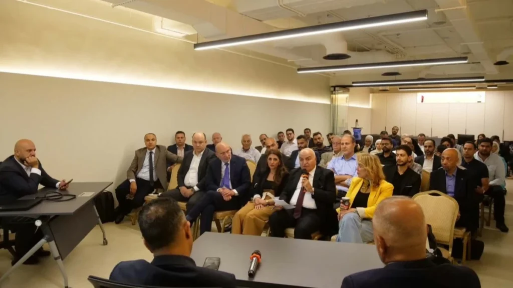 Panel discussion in a conference room with a speaker at a desk and a attentive audience ahead of him.