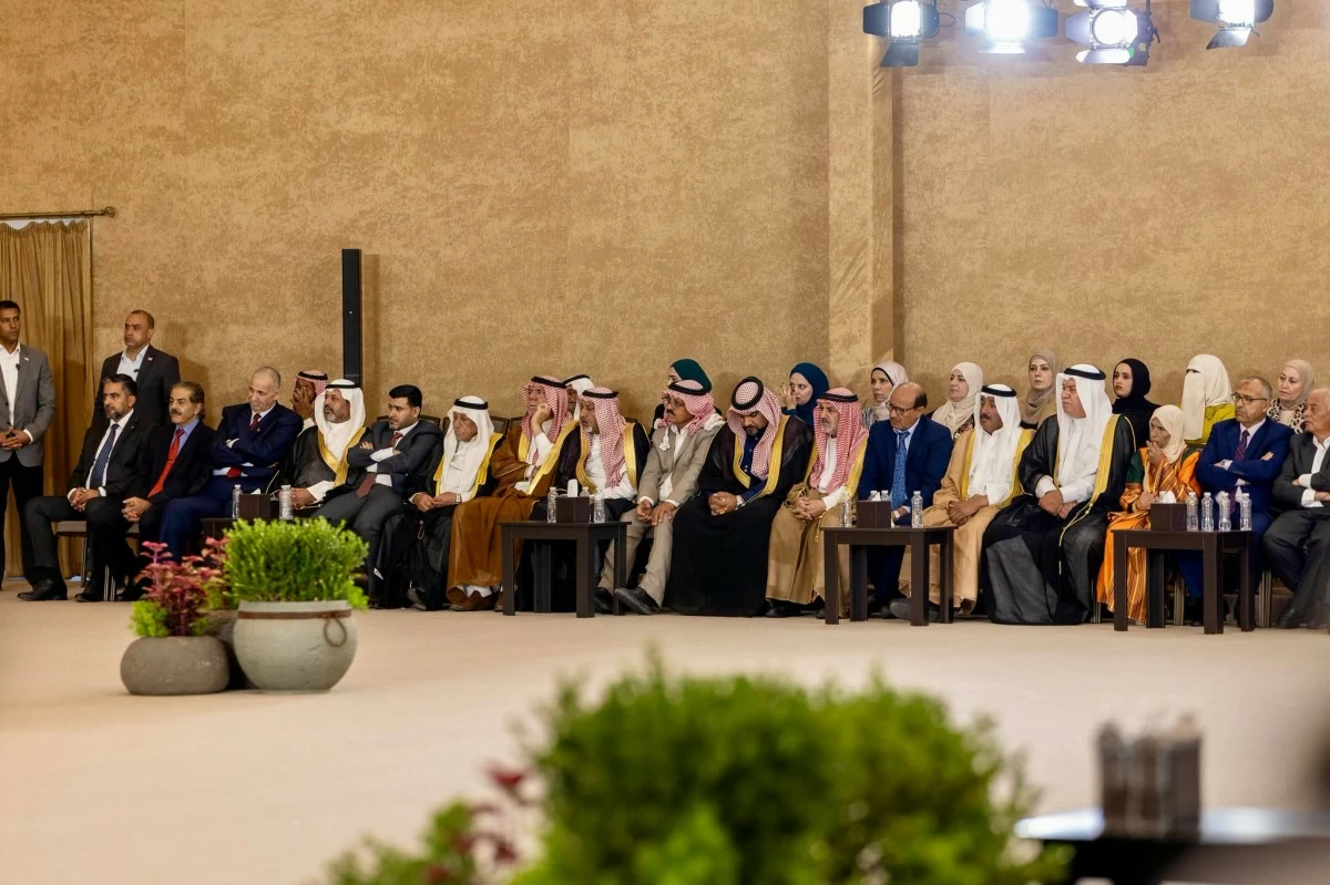 Row of dignitaries in traditional robes and suits seated at a formal ceremony in an auditorium setting.
