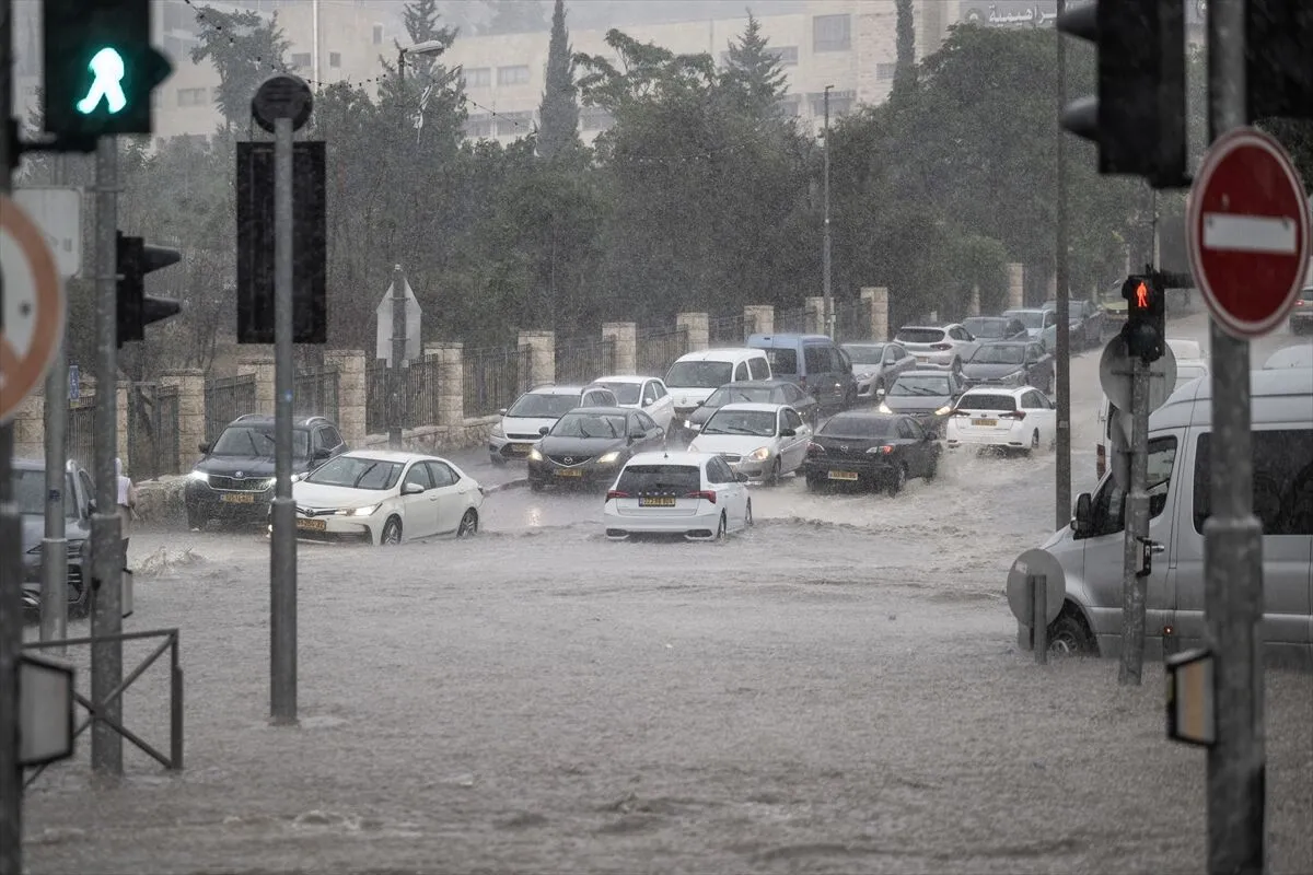 762784 - عروبة الاخباري | Oroba News Cars stuck and driving through a flooded city street during heavy rain at an intersection, with traffic signals visible.