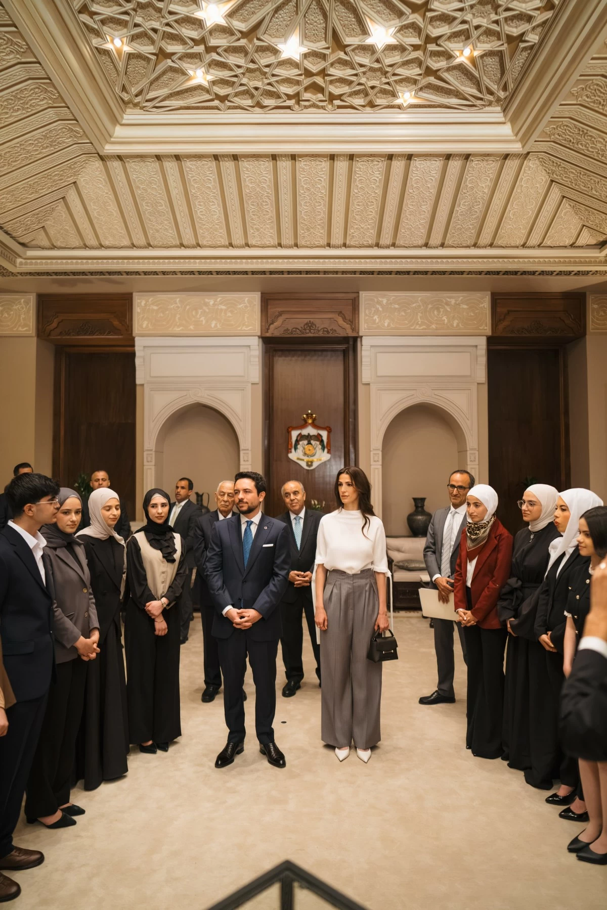 People in business attire stand in a grand, ornately decorated hall; a central woman wears a white blouse and gray pants.