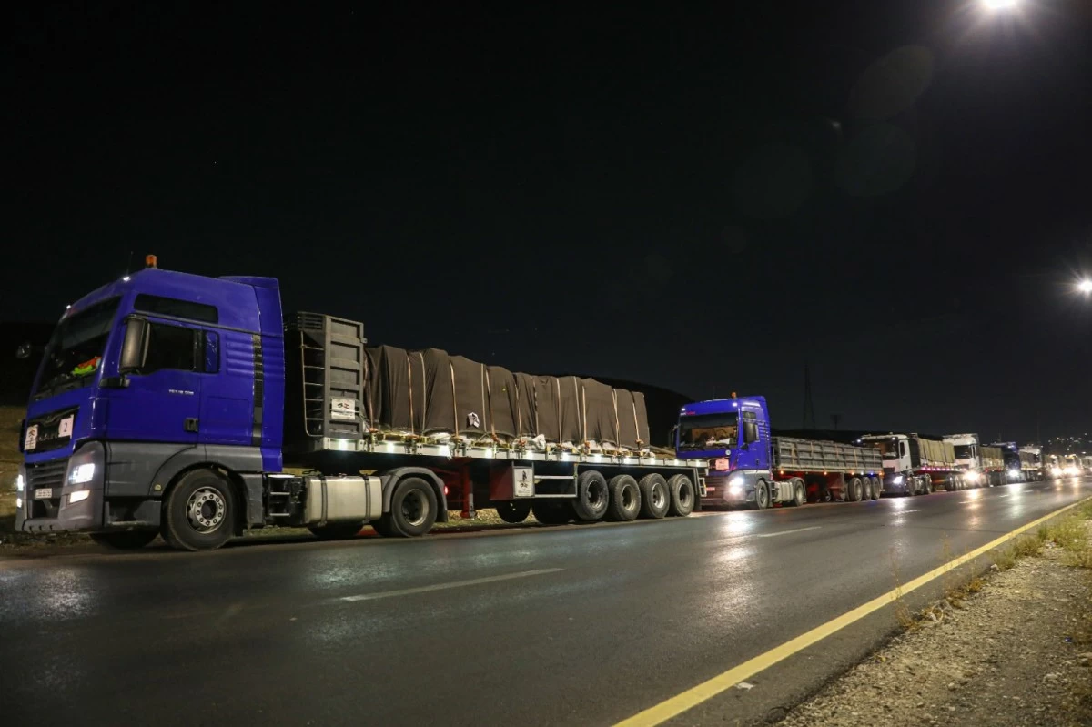 763648 - عروبة الاخباري | Oroba News Line of blue trucks with covered trailers stopped along a dimly lit highway at night.