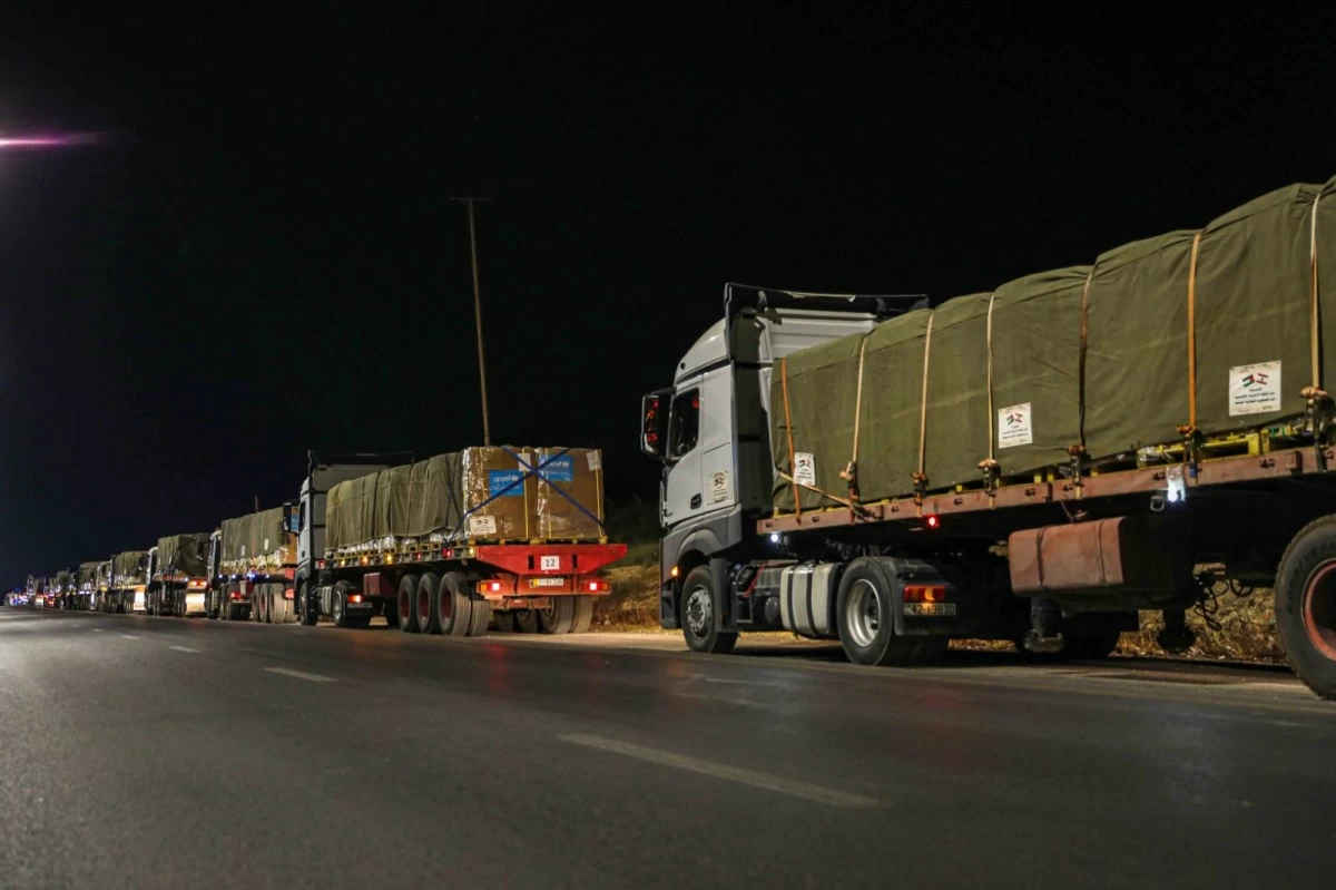 763649 - عروبة الاخباري | Oroba News Nighttime highway with a long line of semi-trucks carrying large green-covered cargo secured with straps along the roadside