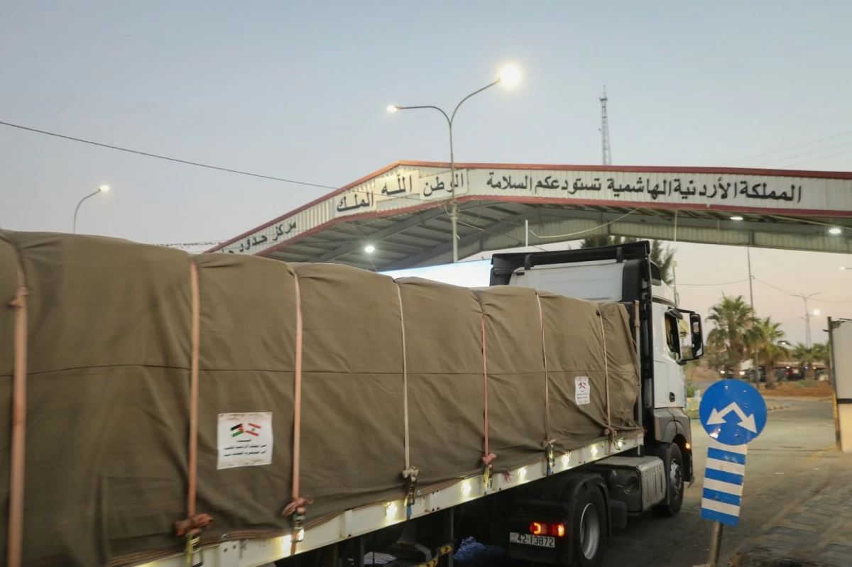 763652 - عروبة الاخباري | Oroba News Large truck with brown tarp-covered cargo at a border checkpoint under an Arabic sign, at dusk/early morning light.