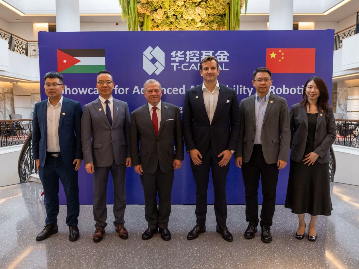Six professionals in business attire pose in front of a blue banner with a company logo, Jordan and China flags, at a ‘Showcase for Advanced Mobility Robotics’ event.
