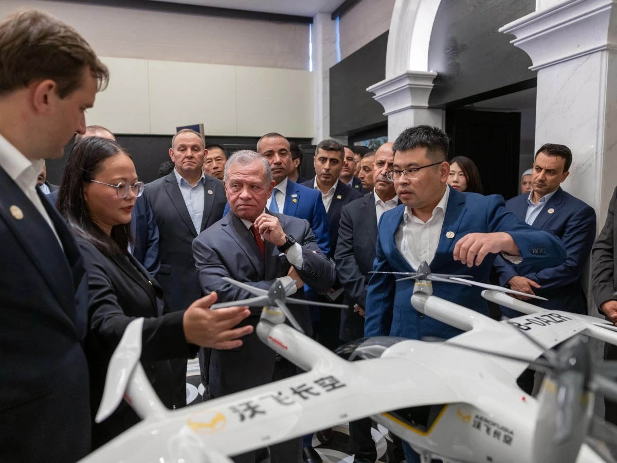Group of professionals in business attire gathered around a white quadcopter drone on display indoors.