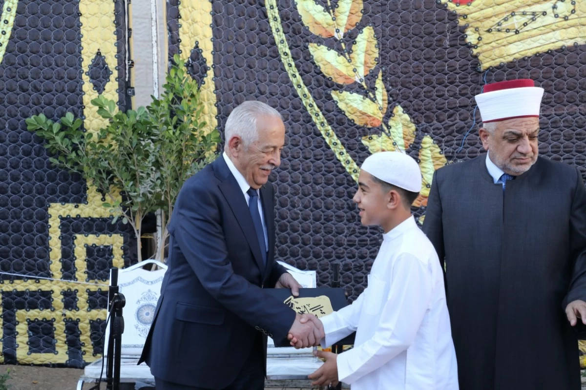 A man in a suit shakes hands with a young boy in traditional white clothing; another clergyman watches nearby as they smile outdoors.