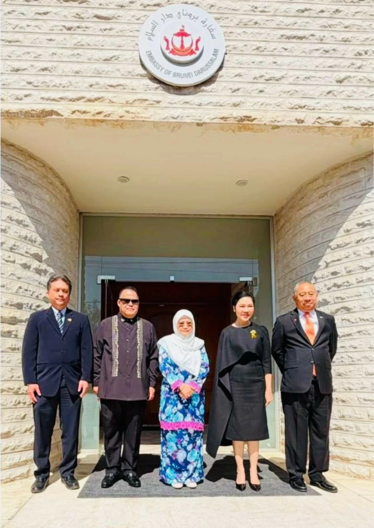 764150 - عروبة الاخباري | Oroba News Group of five formally dressed people posing on the Brunei Darussalam Embassy steps, center woman in a blue floral dress with hijab.