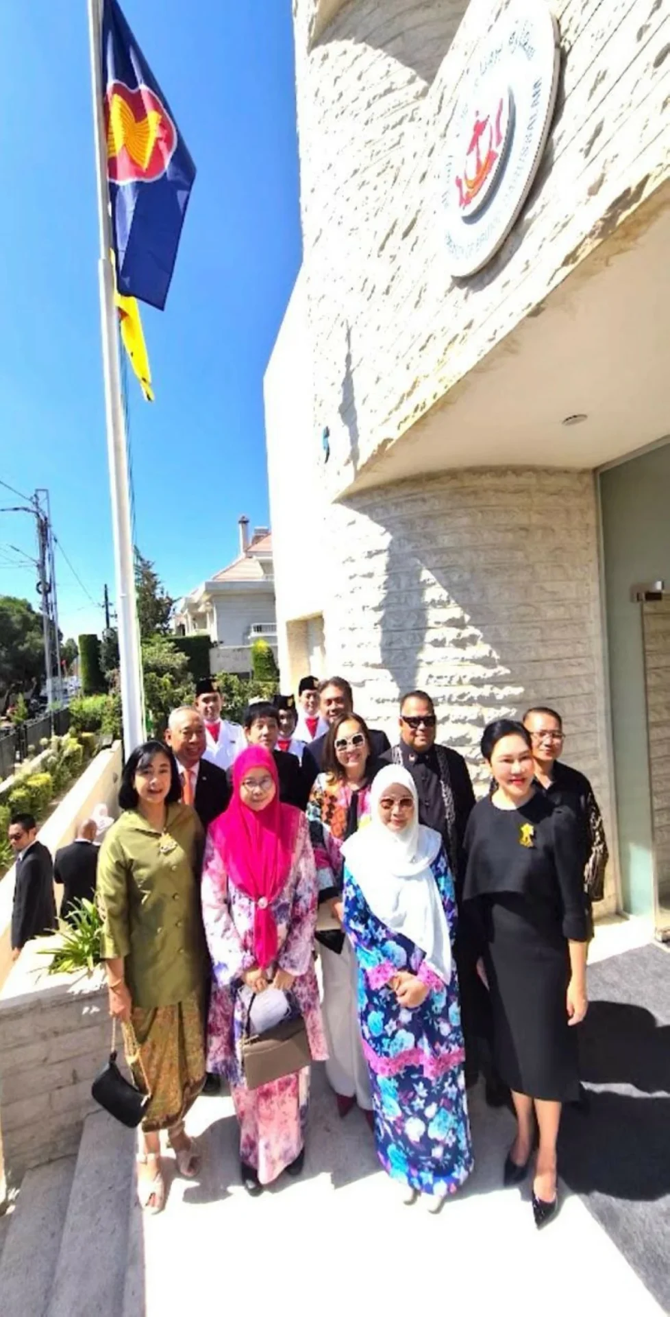 764152 - عروبة الاخباري | Oroba News Group of people in colorful traditional and formal clothing posing outside a stone building with a flag.