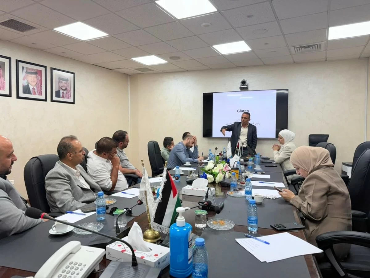 764232 - عروبة الاخباري | Oroba News Business meeting in a conference room with attendees around a long table and a presenter at the front near a screen displaying a slide that says 'Gluten' (possibly a lecture or workshop).