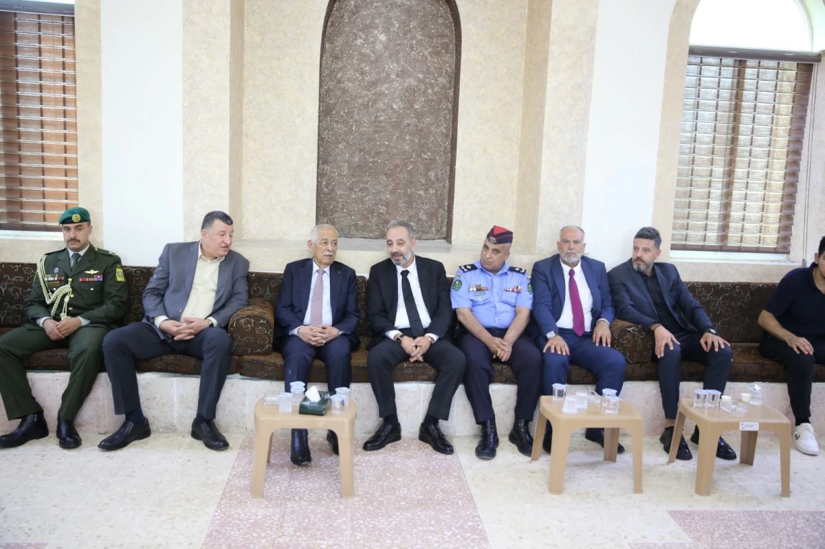 Group of men in formal and military attire seated on a long brown couch in a ceremonial room, with small tables holding water cups in front of them.