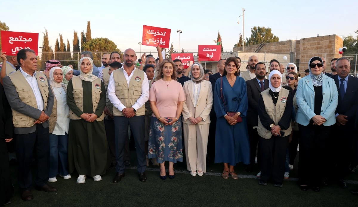 Diverse group of adults wearing beige vests and casual/formal clothing posing outdoors at an event, several holding red Arabic signs overhead or at chest height.