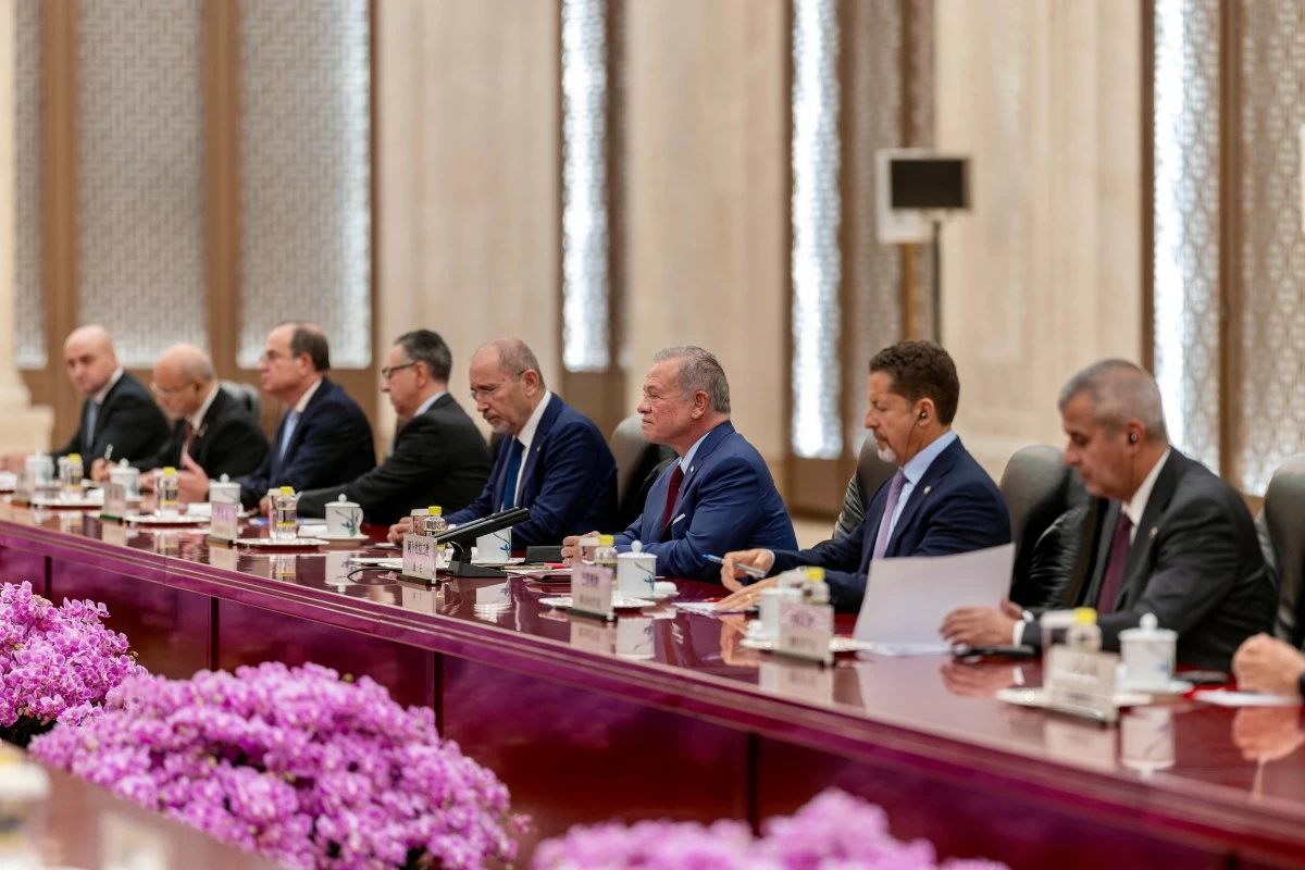 764900 - عروبة الاخباري | Oroba News A group of formally dressed men sit along a long conference table in a meeting room, with pink flowers in the foreground.