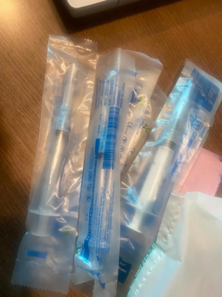 Several sealed syringe packets on a wooden desk, with blue labeling visible around the edges.