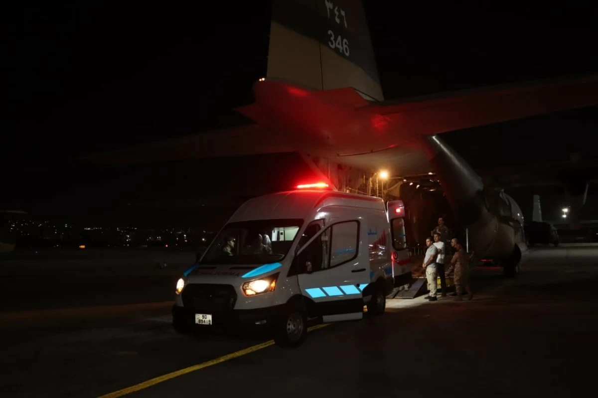Nighttime scene at an airport: an ambulance with blue stripes and red lights parked near a plane with its door open and crew nearby.]