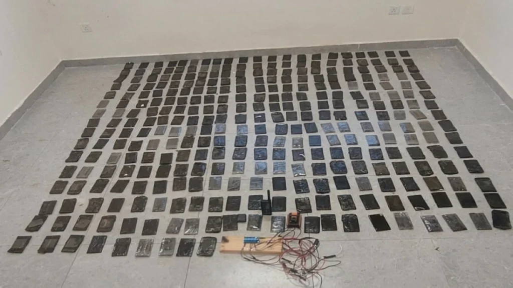 Dozens of mobile phones laid out in neat rows across a tiled floor, with cables and small equipment placed at the front.