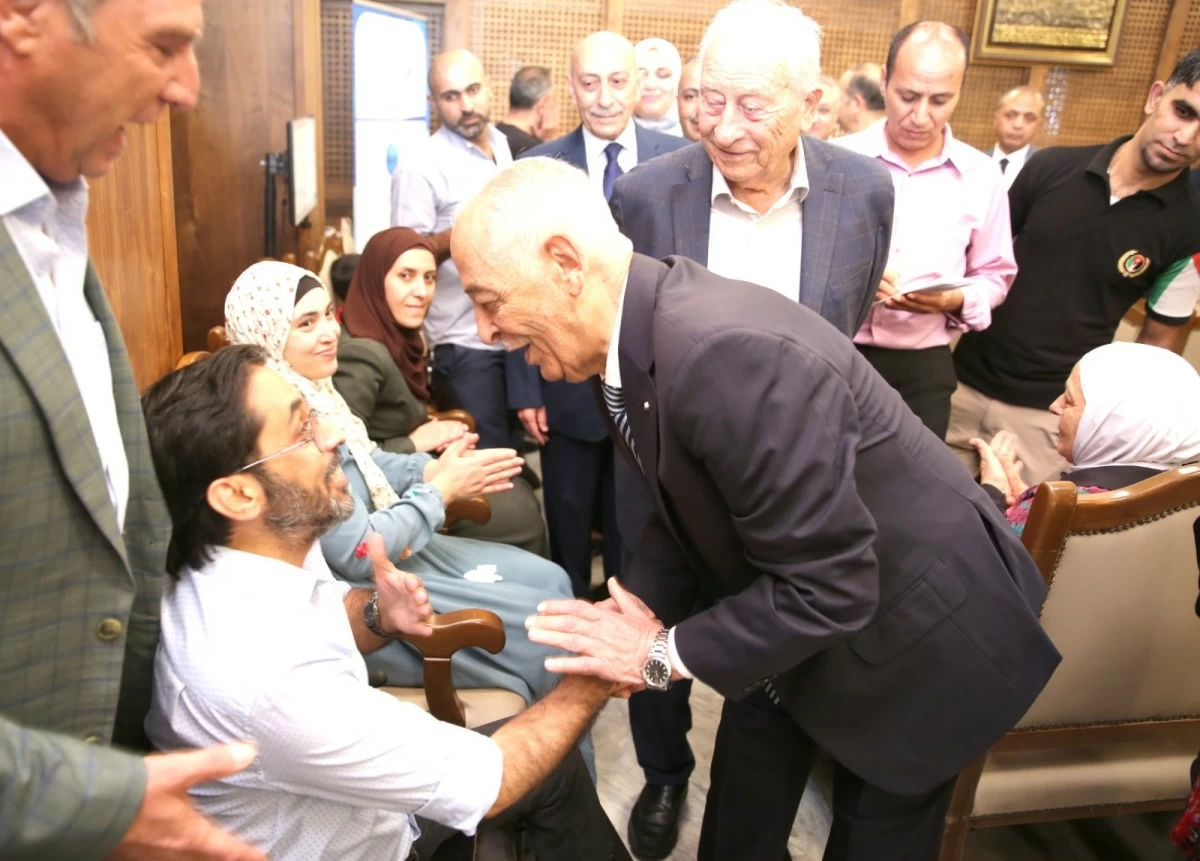766037 - عروبة الاخباري | Oroba News A man in a dark suit leans to greet a seated man with whom he shakes hands at a formal gathering while others look on.