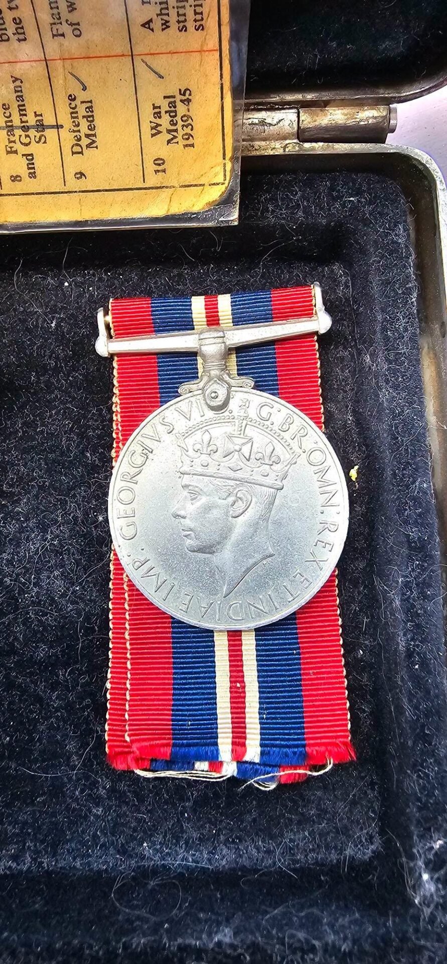 Silver medal featuring King George V in profile with a crown, mounted on a red, blue, and white striped ribbon in a presentation case.