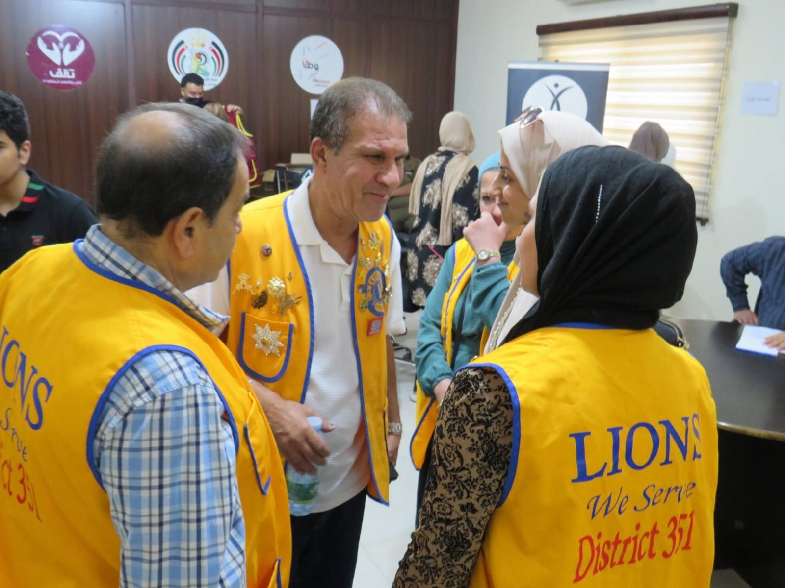 768230428_122373550088016148_9046555566182562314_n - عروبة الاخباري | Oroba News People in bright yellow Lions vests with insignia converse in a room during a community event.