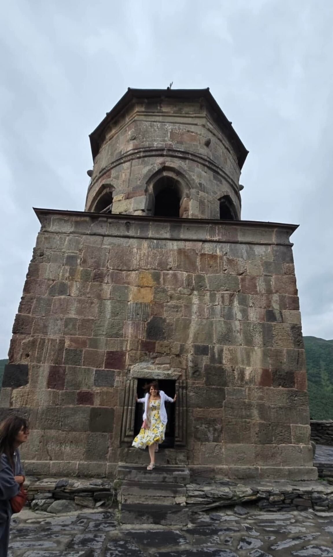 Screenshot - عروبة الاخباري | Oroba News Stone historic tower with arched openings, a doorway at base; a woman in a floral dress steps out of the doorway.