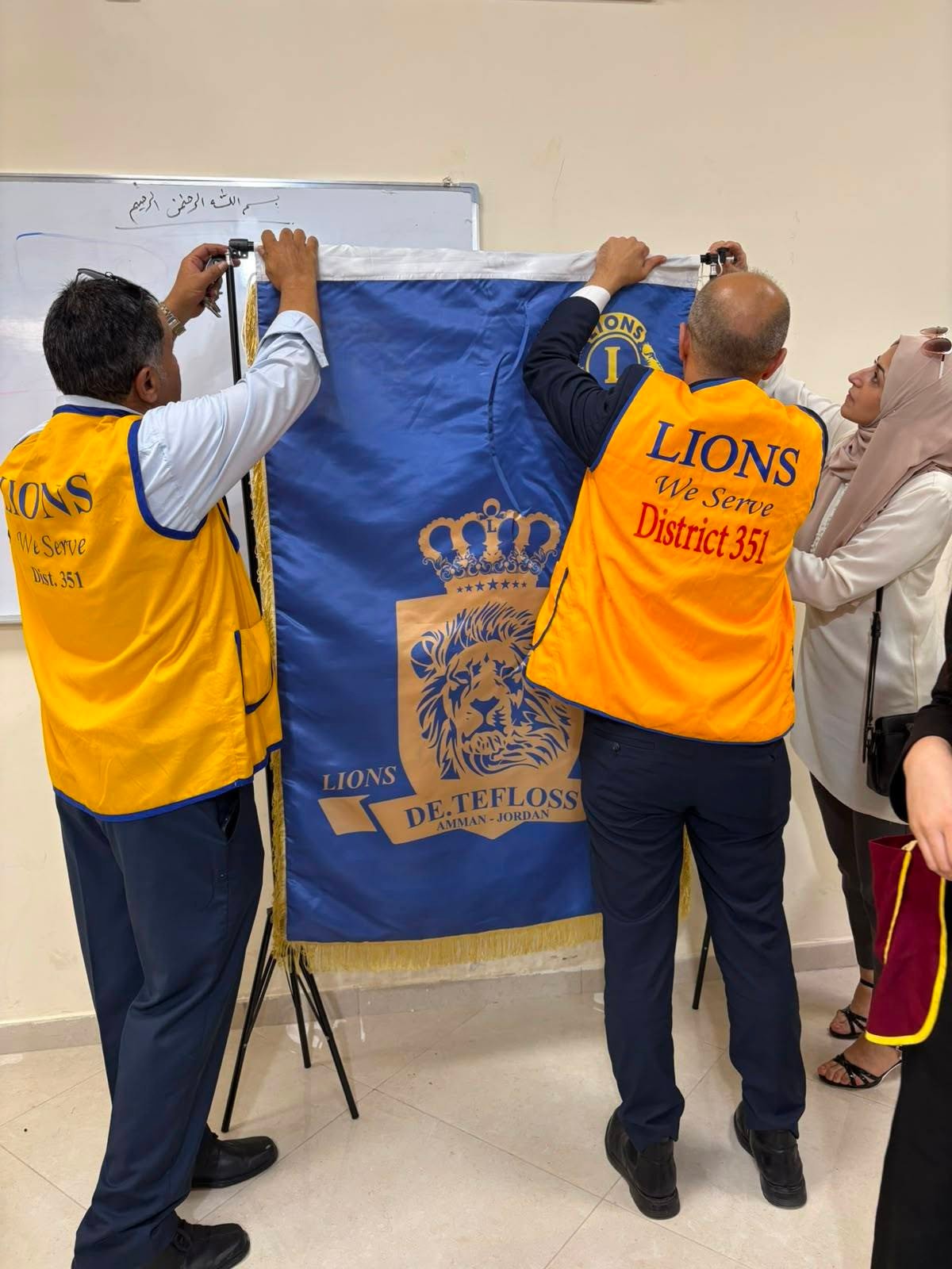 769051745_122373550130016148_3450787108842910266_n - عروبة الاخباري | Oroba News Group of Lions club volunteers unveiling a blue banner with a lion crest; vests read 'LIONS We Serve District 351'