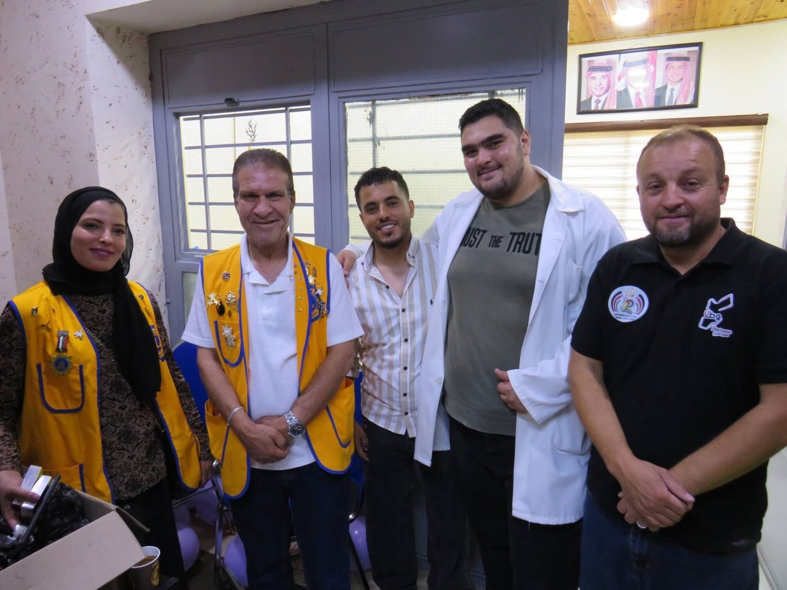 769051768_122373550640016148_5762366426621437843_n - عروبة الاخباري | Oroba News Five people pose for a group photo indoors: two wearing yellow vests with badges, others in casual or lab attire, smiling at the camera.